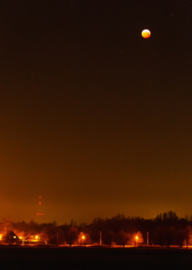 06:41 MEZ, ISO 3200, 1.6sec, F5.6, 100mm. Der Mond wandert Richtung Horizont, s. d. jetzt auch der Horizont in das Bild mit einbezogen werden kann. Links unten sieht man den Sendeturm Geitelde, davor befindet sich der Ortsteil Braunschweig-Stöckheim. Die Totalität ist gleich zuende.